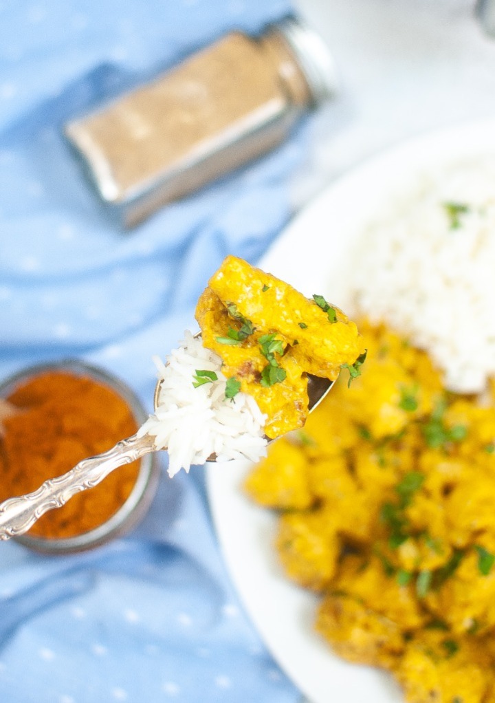 A forkful of curry chicken with a scoop of rice over a dinner plate. 