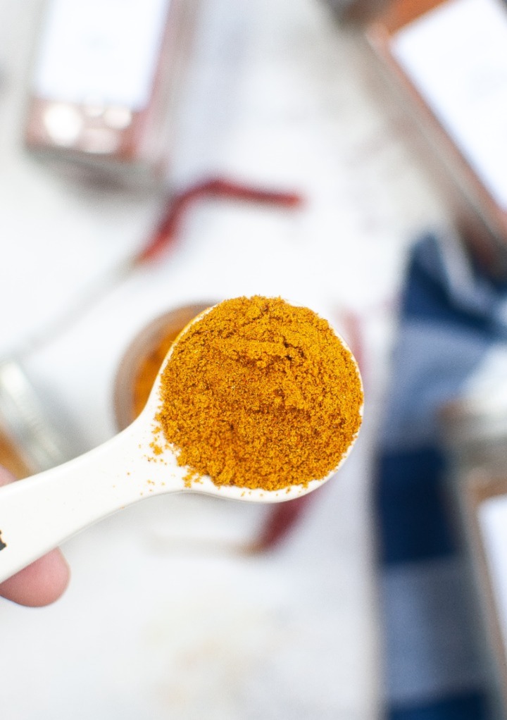A close view of curry powder in a white measuring spoon. 