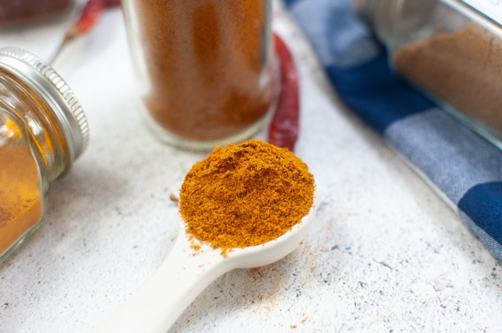 Homemade diy curry powder mix with the powder in a white measuring spoon.