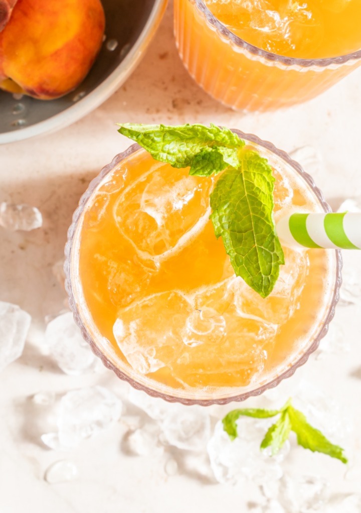 Overhead view of a glass of peach tea with ice with mint leaves. 