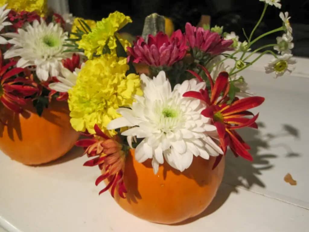 DIY pumpkin centerpiece for decoration filled with yellow, white and purple flowers. 
