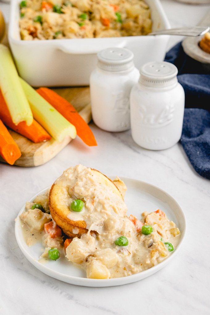 A white plate topped with a popover and creamy chicken with a casserole dish in the back. 