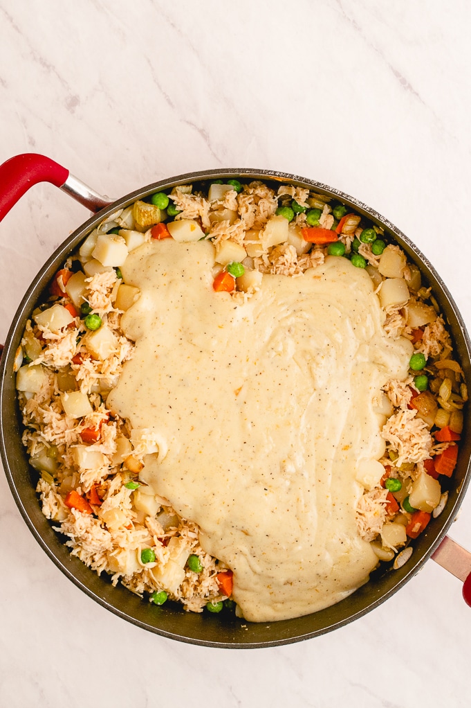 Skillet topped with cream sauce covering chicken and vegetables.