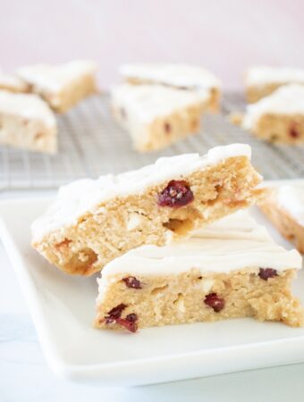 Sliced cranberry bliss bars on a white plate with a backing rack in the background with more bars.
