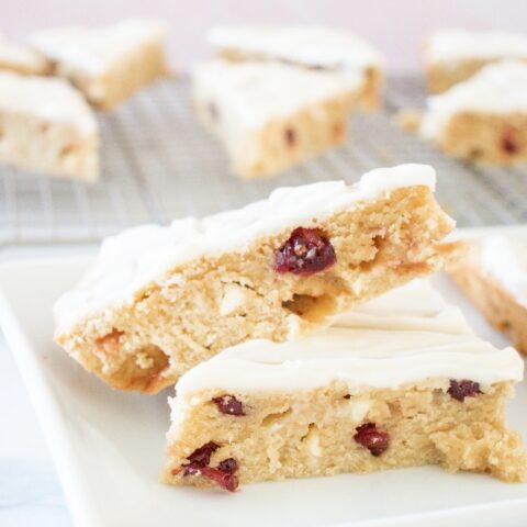 Sliced cranberry bliss bars on a white plate with a backing rack in the background with more bars.