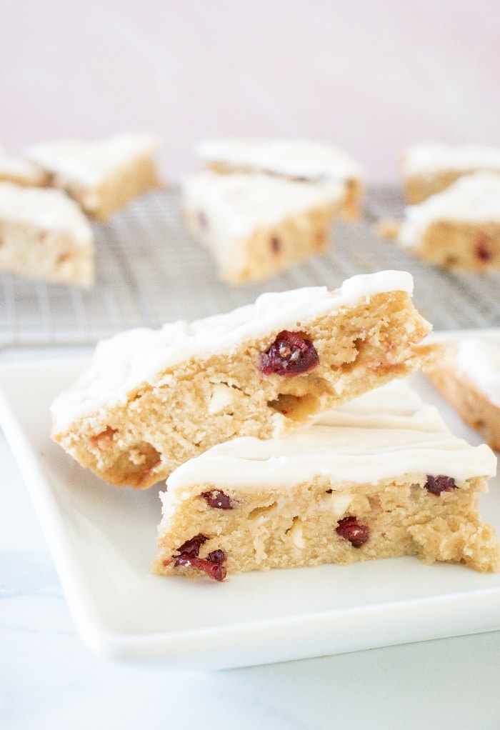 Sliced cranberry bliss bars on a white plate with a backing rack in the background with more bars. 