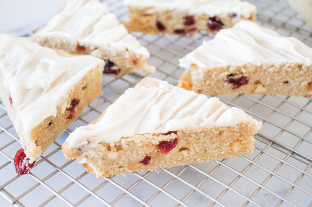 Sliced cranberry bliss bars frosted with sweet cream cheese on a cooling rack. 