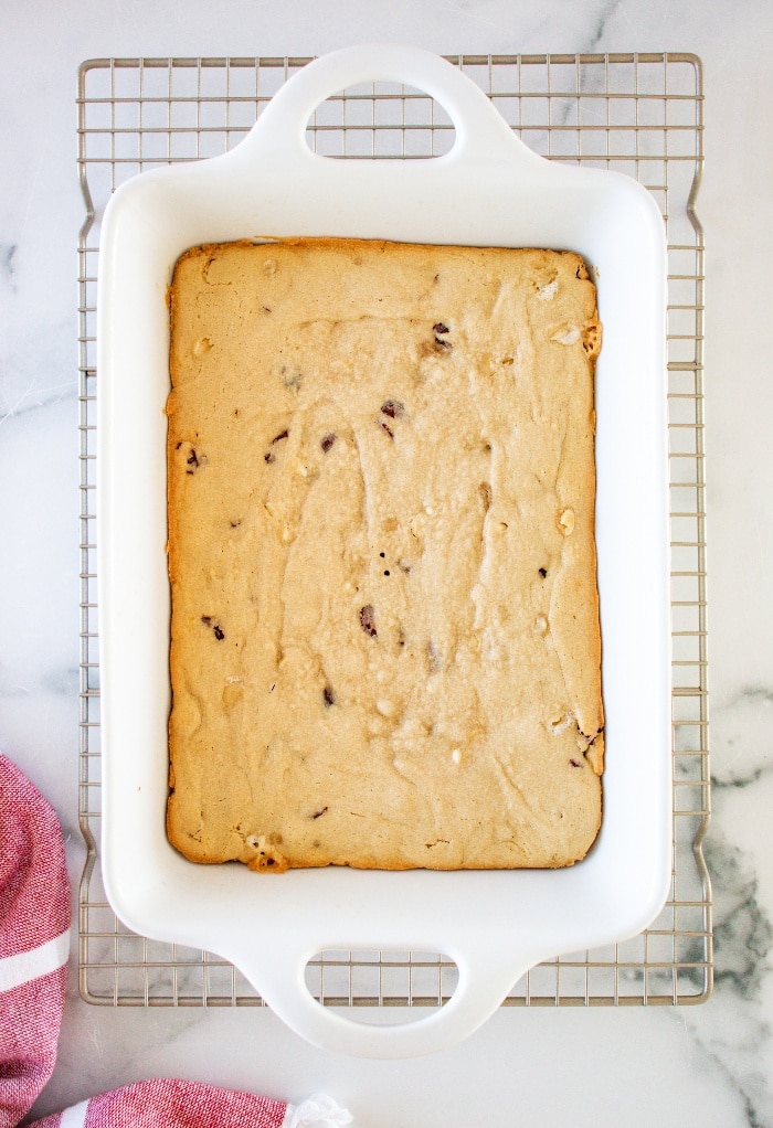 Baked cookie bar in a white baking dish cooling on a baking rack.