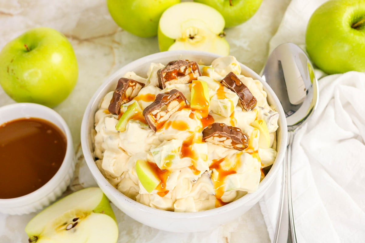 Apple Snickers salad in a white bowl with green apples on the side.