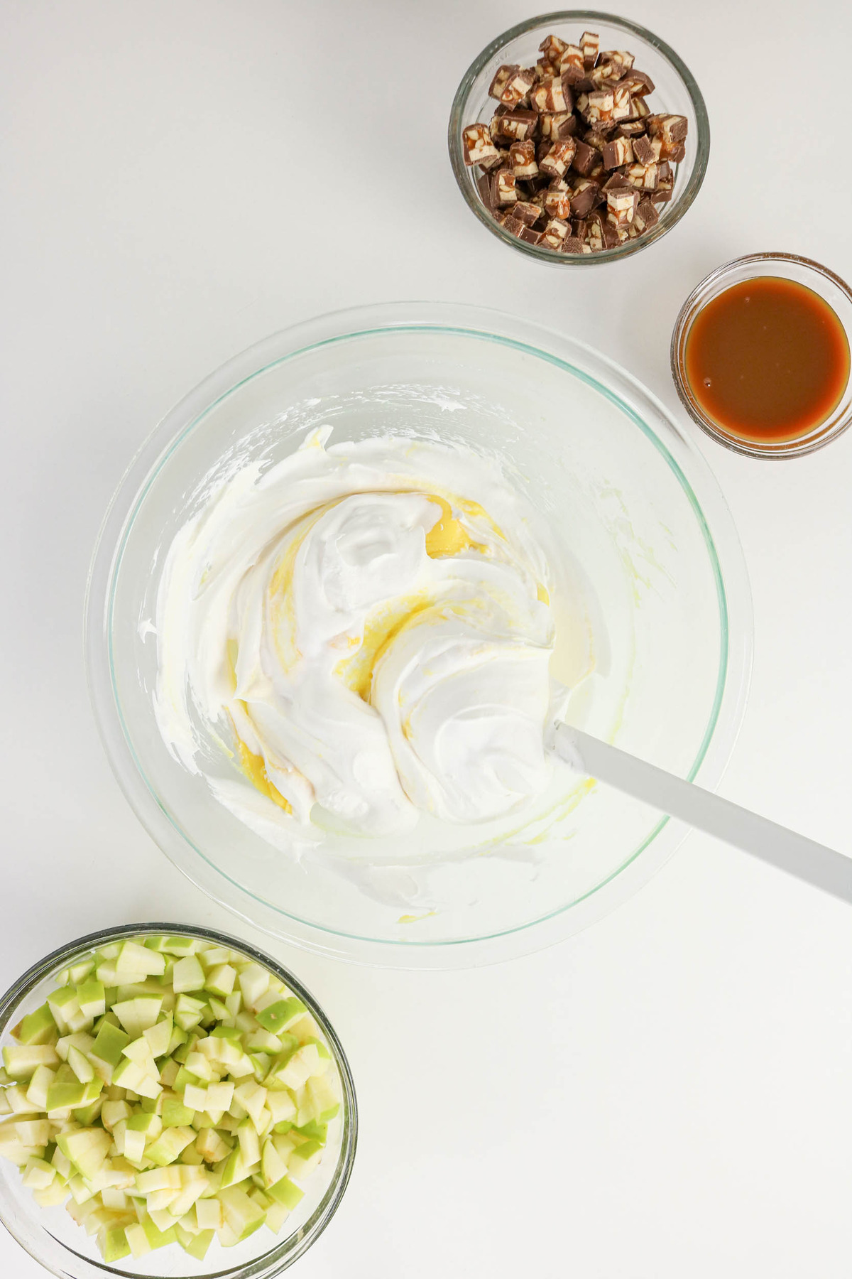 Whipped cream added to pudding mix in a clear mixing bowl.