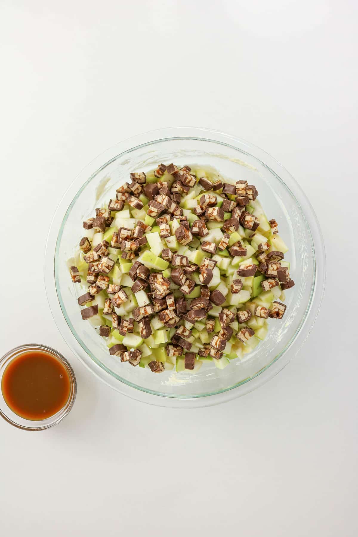 Diced Snicker candy and diced apples in a mixing bowl with vanilla pudding and whipped cream.