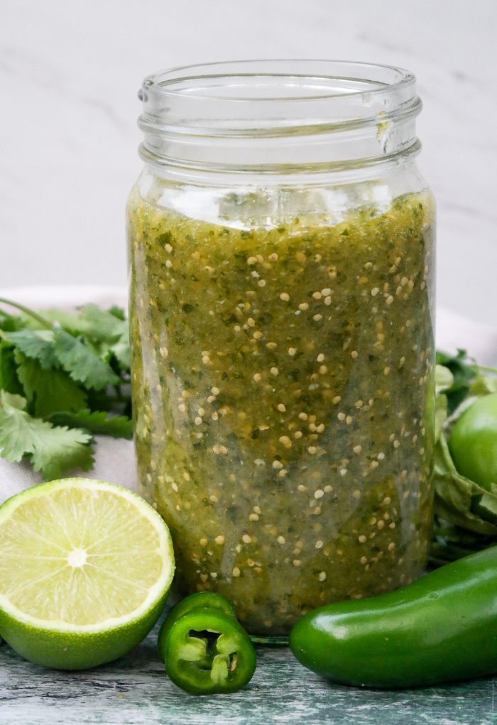 A clear jar of homemade salsa verde with a sliced line on the side with a jalapeno. 