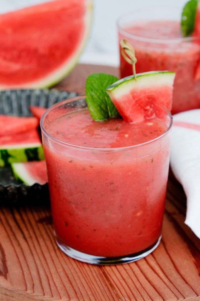 Watermelon cooler in a clear glass with a mint sprig and watermelon slice. 