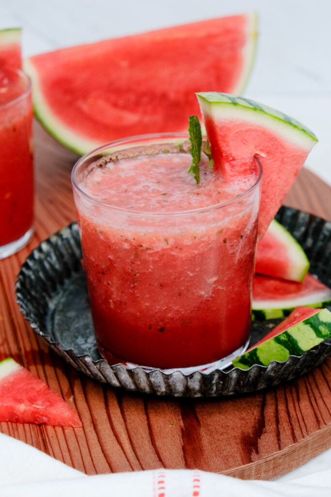 Fruit slushy in a clear glass sitting in a tin coaster. 