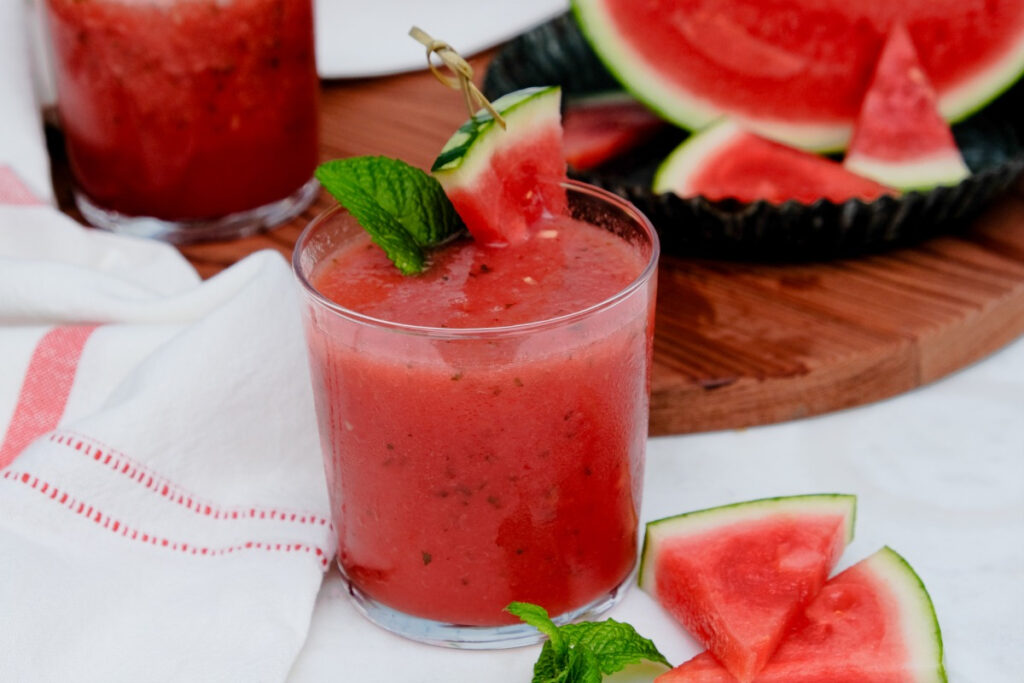 Drink on a white table with sliced watermelon on the side. 