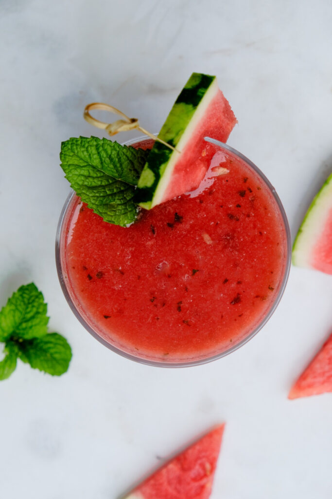 Overhead view of a glass with blended watermelon and garnished with mind and a slice of watermelon. 