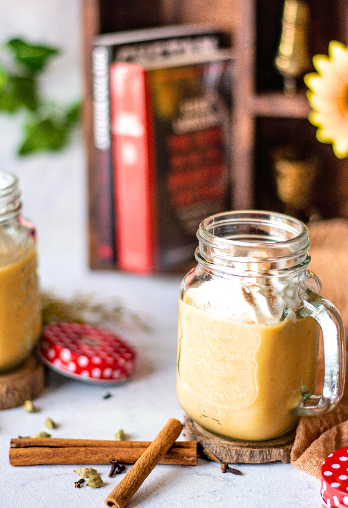 Pumpkin smoothie in a clear glass with cinnamon sticks on the side. 