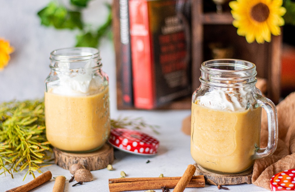 A horizontal view of two pumpkin smoothies in mason jars with handles. 