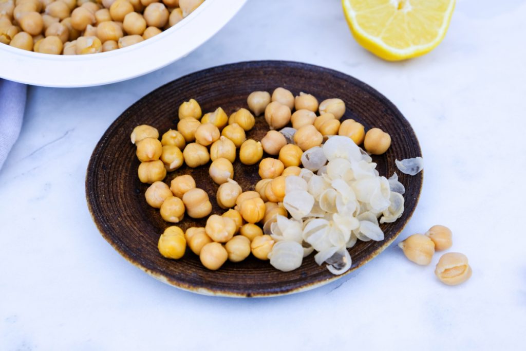 Removing the skin from the chickpea and placing the beans on a brown plate. 