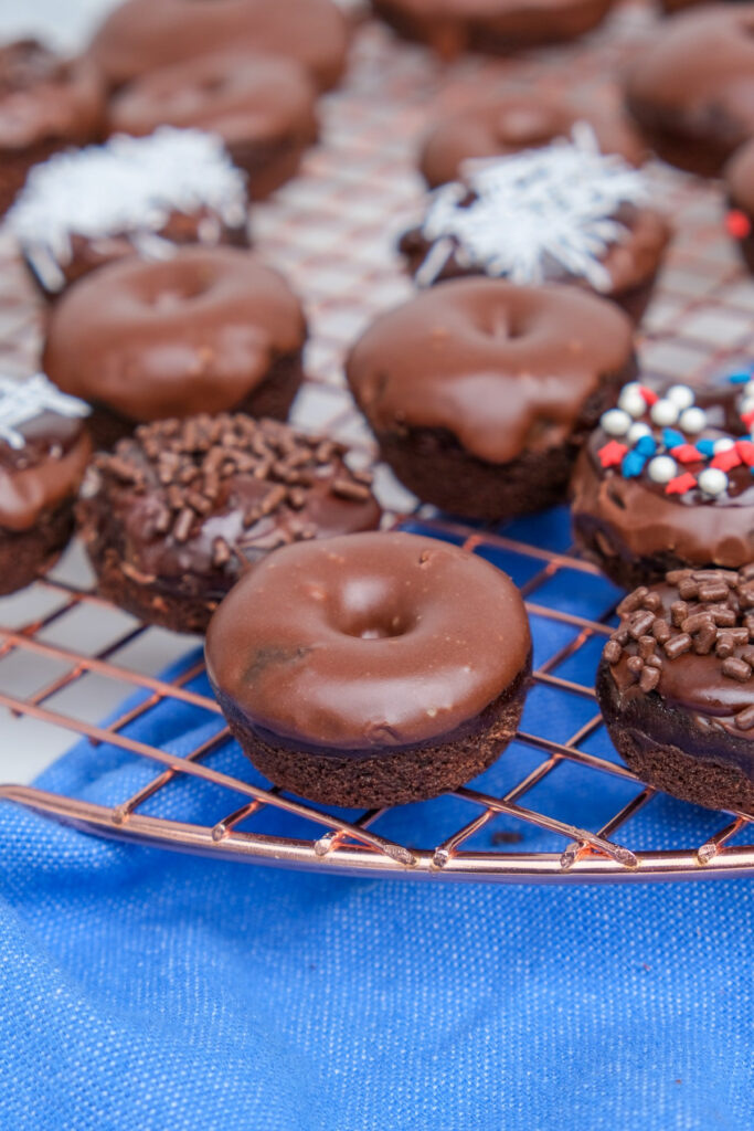 A variety of mini chocolate donuts on a cooling rack.