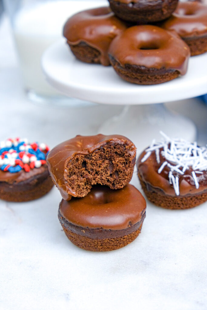 Two chocolate donuts placed on top of each other with a bite taken out of one. 