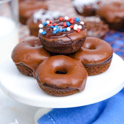 Mini chocolate donuts on a small white cake plate.