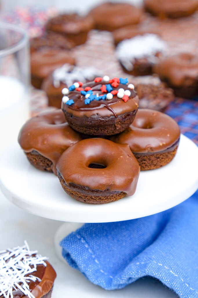 Mini chocolate donuts on a small white cake plate.