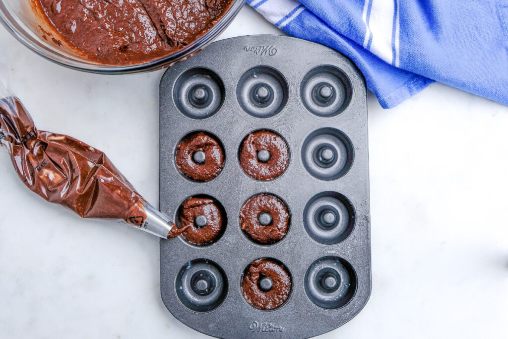 Mini chocolate donut batter piped into a donut pan before baking. 