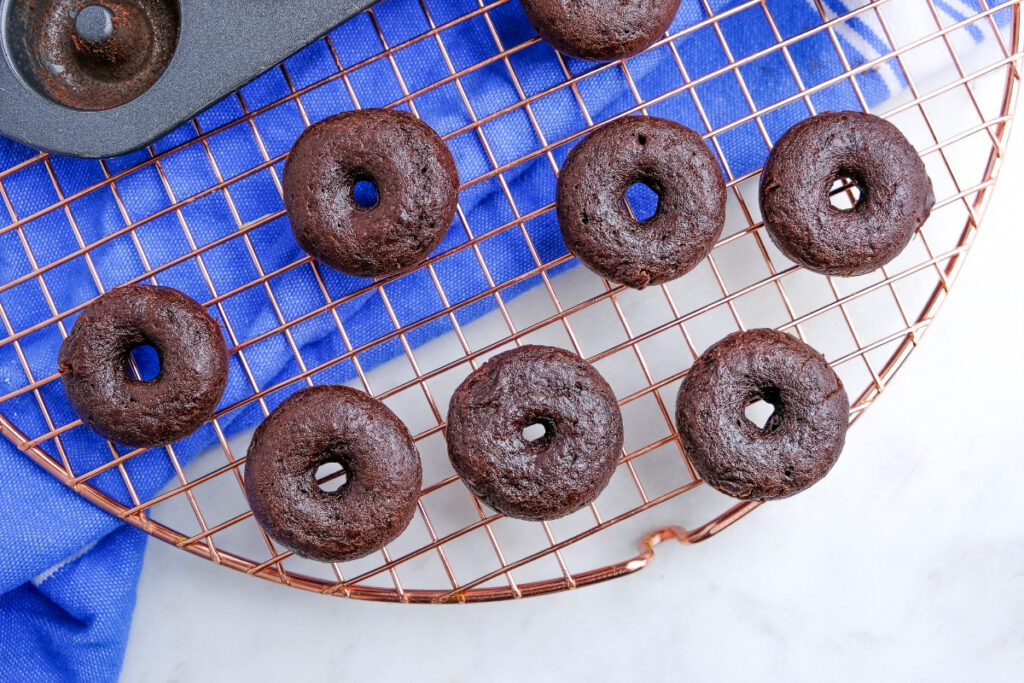 Mini baked chocolate donuts cooling on a baking rack. 