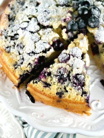 Blueberry coffee cake topped with powder sugar on a white cake plate