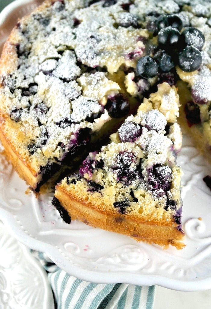 Blueberry coffee cake topped with powder sugar on a white cake plate