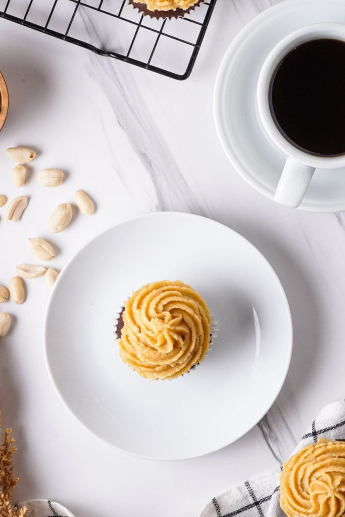 Overhead view of a cupcake on a white dish with a cup of coffee on the side. 