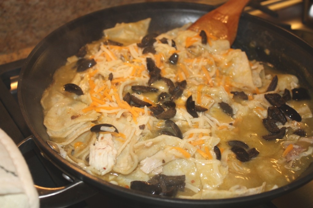 Black skillet with enchiladas topped with olives.