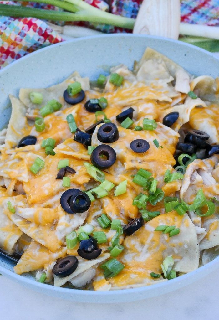 A light blue skillet with enchiladas topped with olives. 