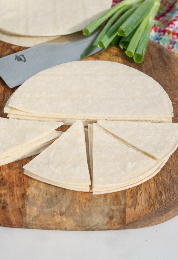 Corn tortillas on a wood cutting board cut into triangles.