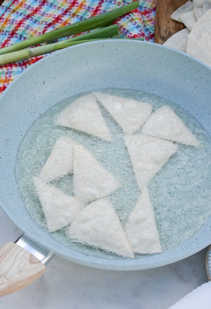 Pan fried corn tortillas in a blue skillet frying.