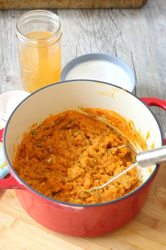 Sweet potatoes being mashed into the mixture for sweet potato soup with coconut milk. 