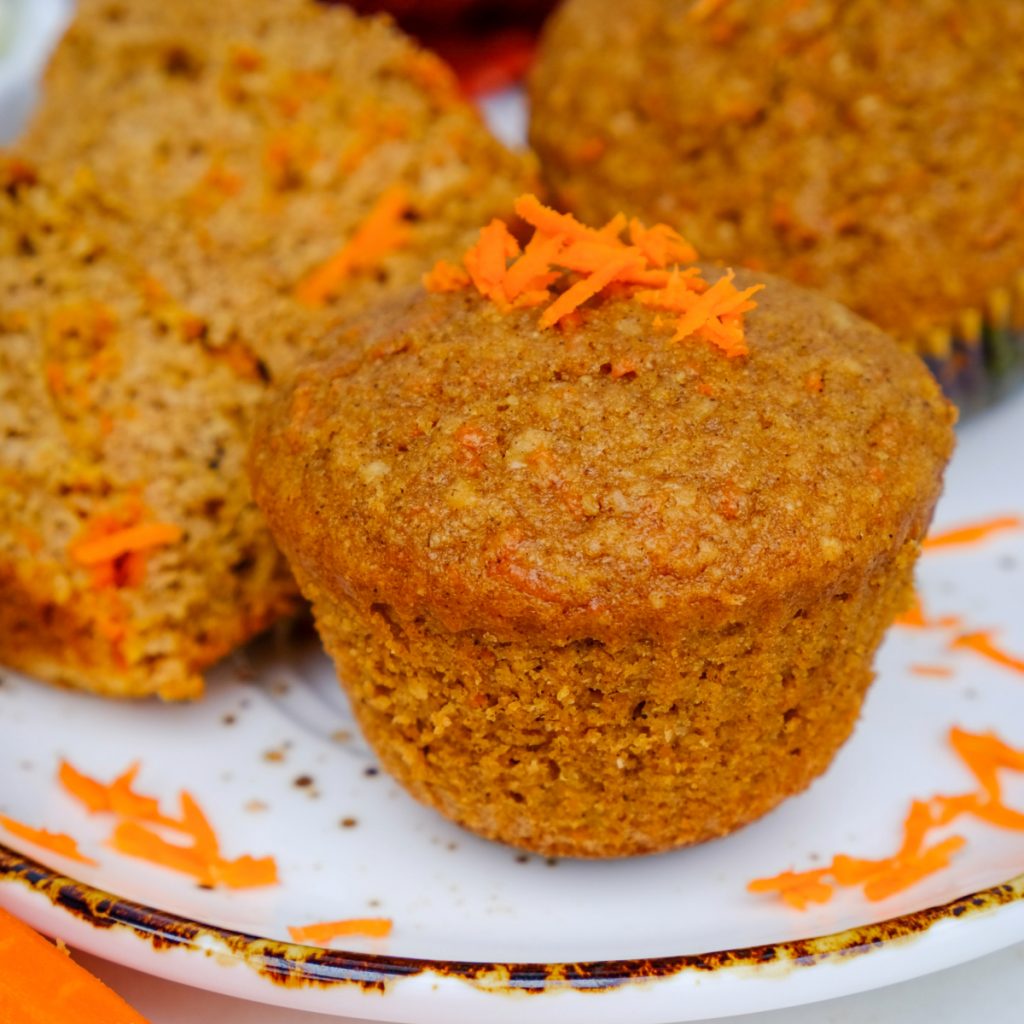 Healthy carrot cake muffin on a serving plate topped with shredded carrots.