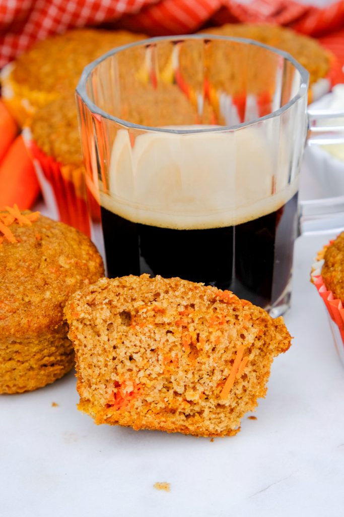 Carrot cake muffin sliced in half next to a cup of coffee ready to enjoy.