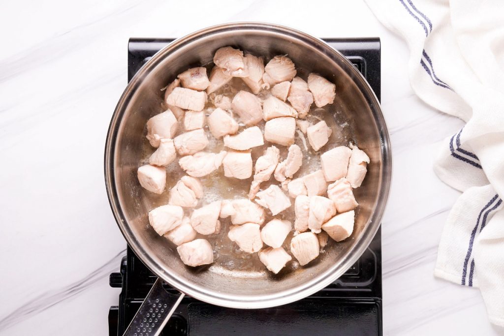 Diced chicken sautéing in a large skillet. 