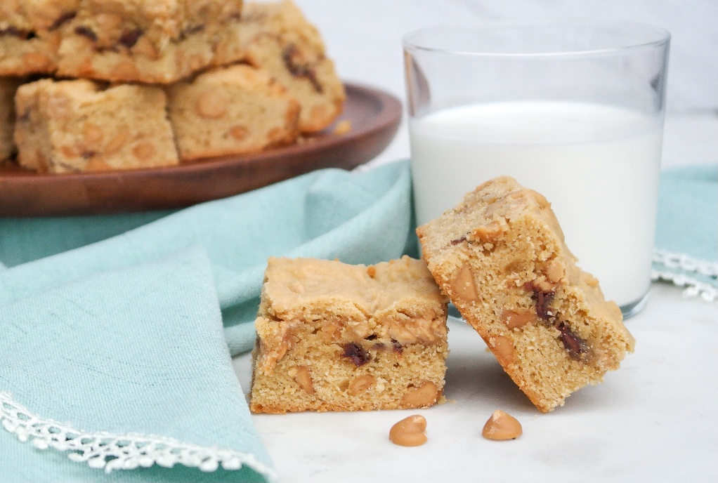 Peanut butter cookie bars with a clear glass of milk.