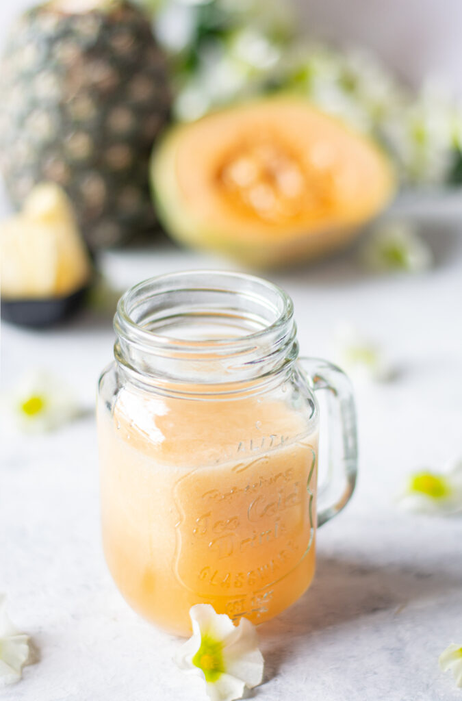 Blended pineapple melon smoothie with fresh fruit in the background