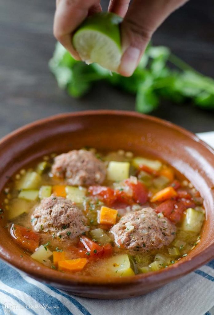 Albondigas soup in a brown bowl with fresh lime juice squeezed over the food