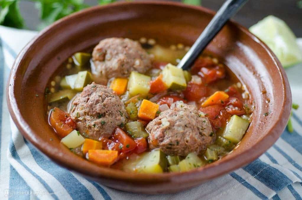 Mexican meatball soup in a brown bowl with a gray spoon