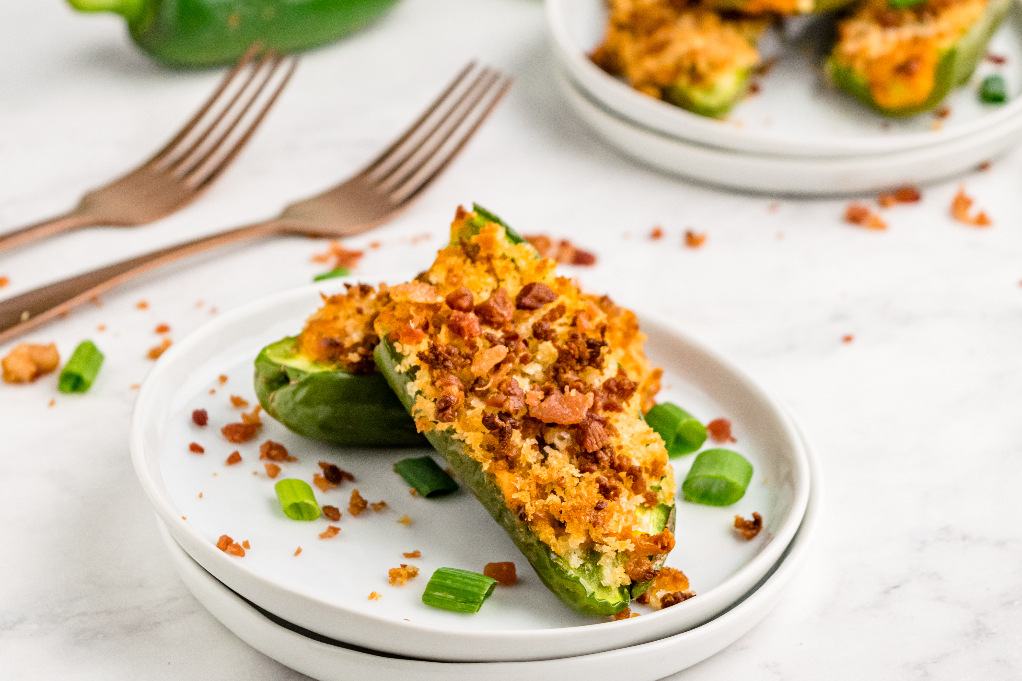 Jalapenos stuffed with cheese and topped with bacon on serving plate.