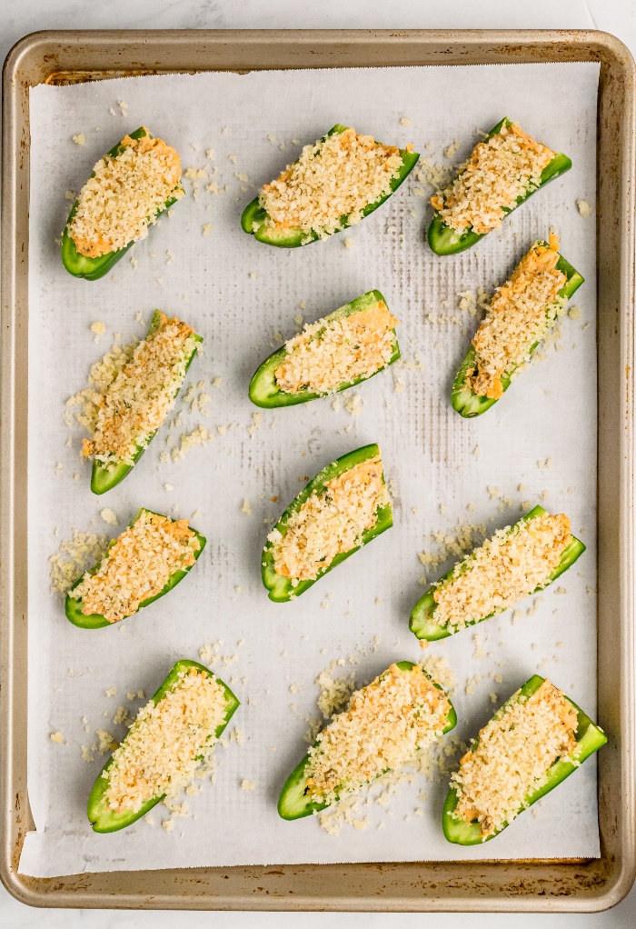 Halved stuffed jalapenos with cheese on a baking sheet.