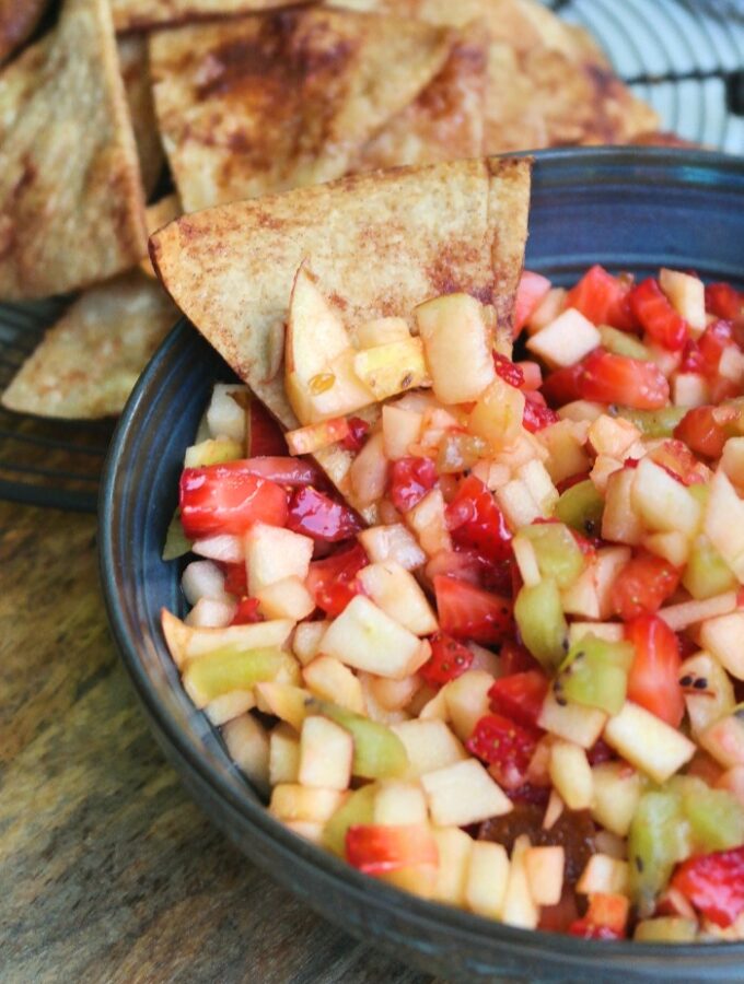 A cinnamon tortilla chip dipped in a fruit salsa bowl.