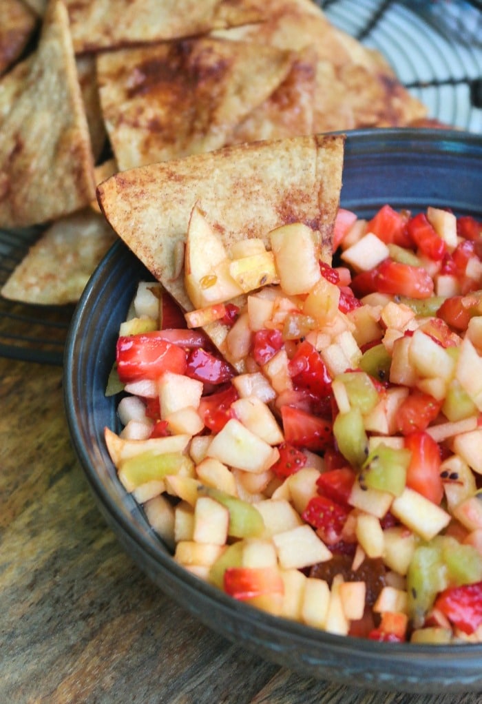 A cinnamon tortilla chip dipped in a fruit salsa bowl.