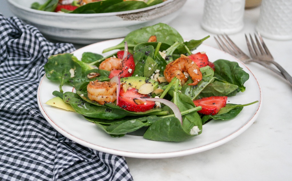 Spinach avocado salad with shrimp on a white salad dish. 