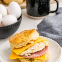 Biscuit sandwich on a white plate filled with egg, ham and cheese.